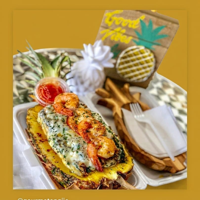 Shrimp and cheese baked in a pineapple half, with a side of sauce and cutlery.